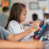 Một học sinh nhỏ tuổi sử dụng iPad với bút cảm ứng trong lớp học.