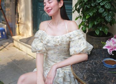 Thùy Tiên xuống phố cà phê cùng bạn bè cùng chiếc váy hoa nhí có gam màu trang nhã. Thiết kế xếp bèo nhún buộc dây giúp hoa hậu tôn phần xương quai xanh.